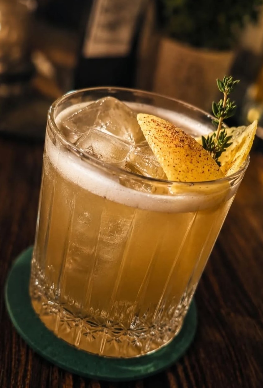 Whiskey Sour mit Thymianzweig und geröstetem Zitronenzest im geschliffenen Tumbler